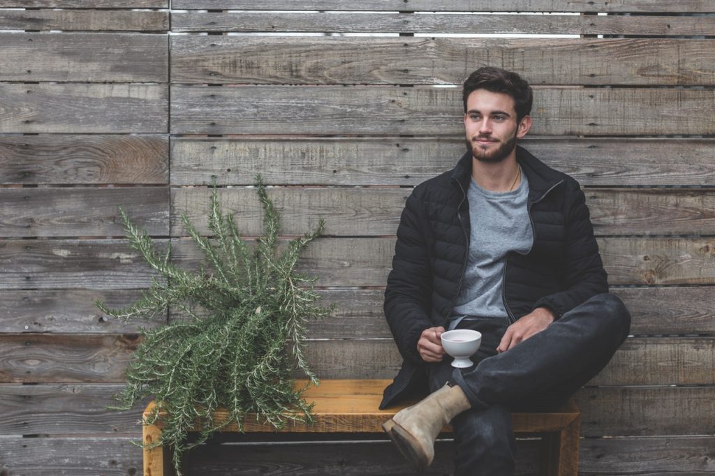 jeune homme assis sur un banc à côté d'une plante et tenant une tasse